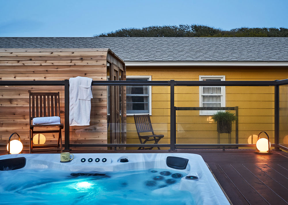 Hot tub on elevated deck with glass railing and outdoor sauna.