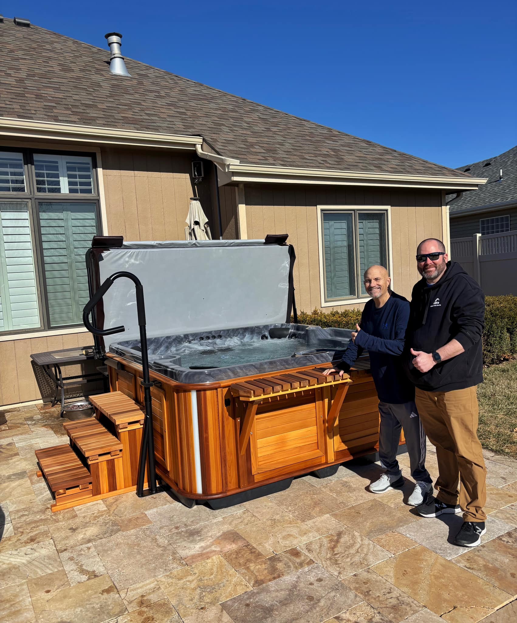 Two men standing beside newly installed hot tub on backyard patio.