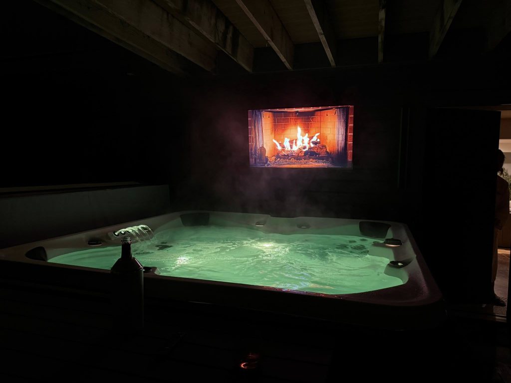 Indoor hot tub with steam rising beneath a lit fireplace.