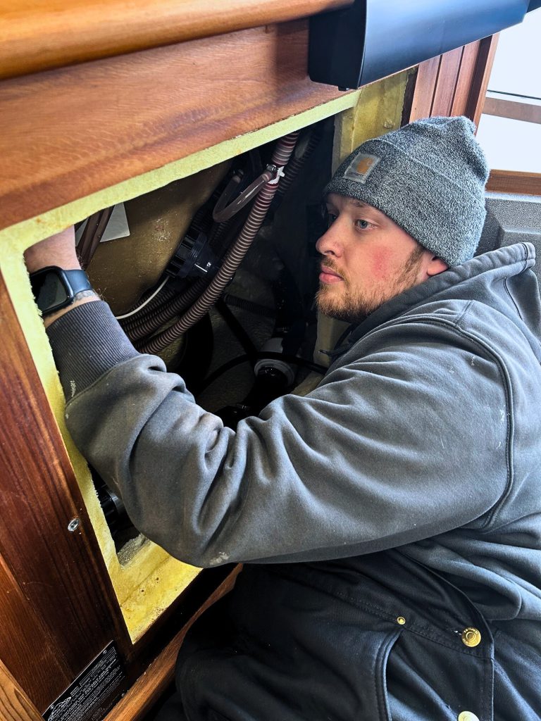 Worker repairing equipment inside a wooden compartment with wiring, supporting maintenance for hot tubs in Topeka.