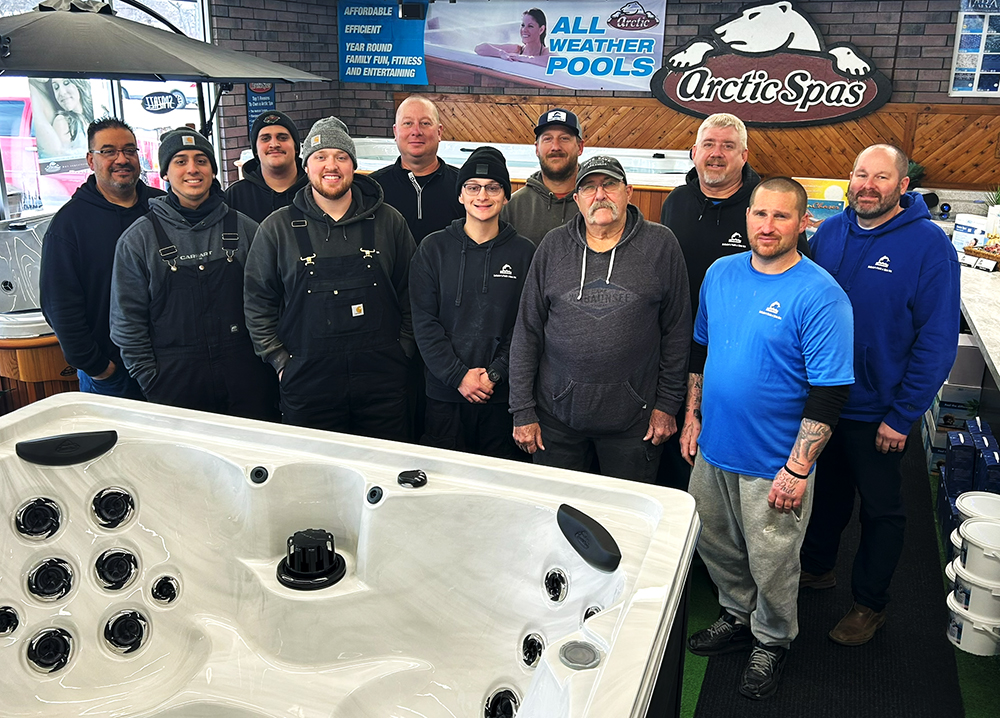 Team posing behind a large showroom hot tub, representing experts for hot tubs in Topeka.