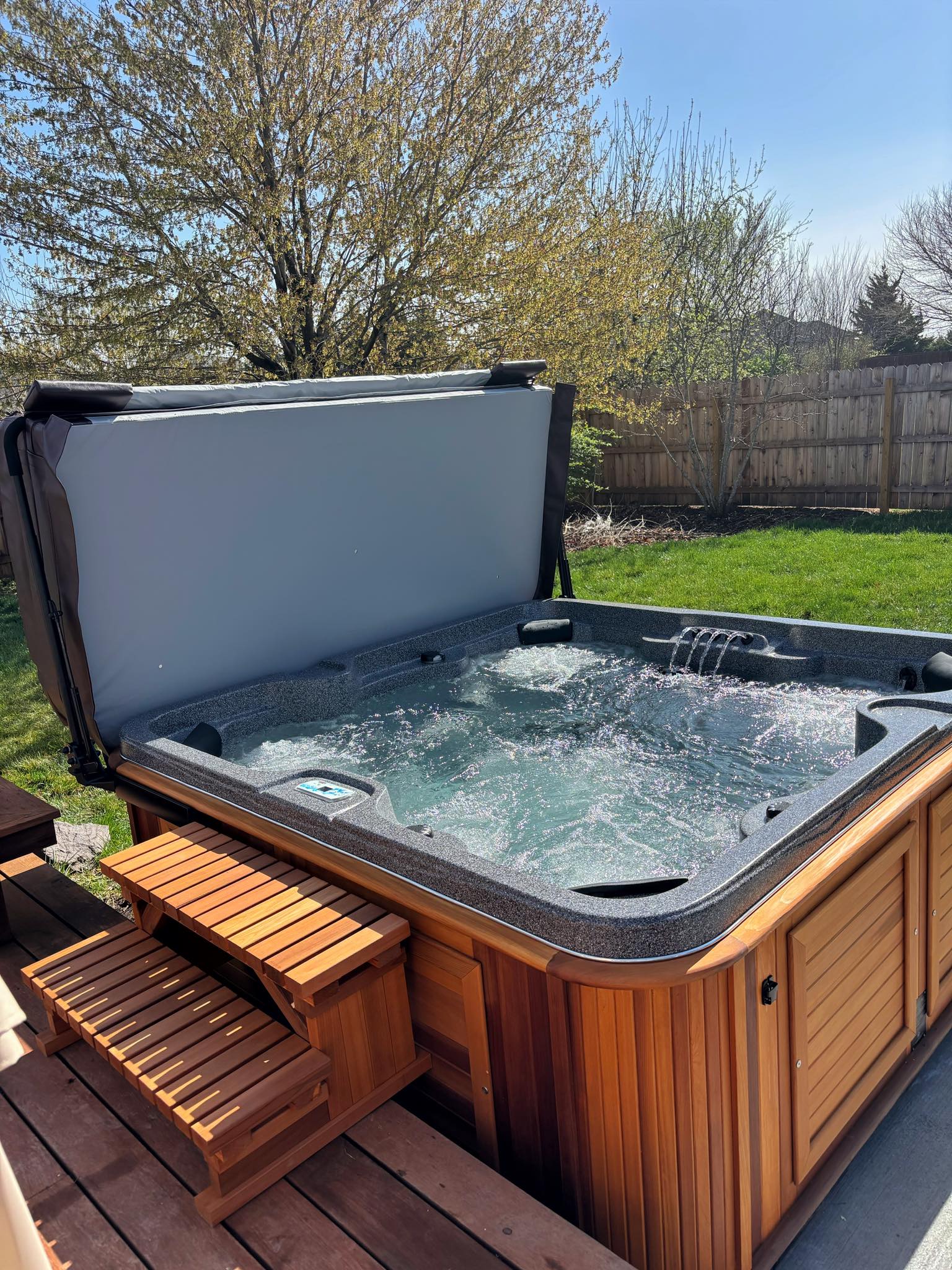 Open outdoor hot tub with bubbling water and wooden steps on a backyard deck.